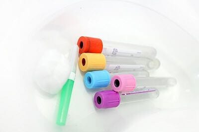Unlabelled pathology phlebotomy, blood collecting vacutainer tubes a 21 gauge needle and cotton wool lying in a kidney dish for a blood collection procedure